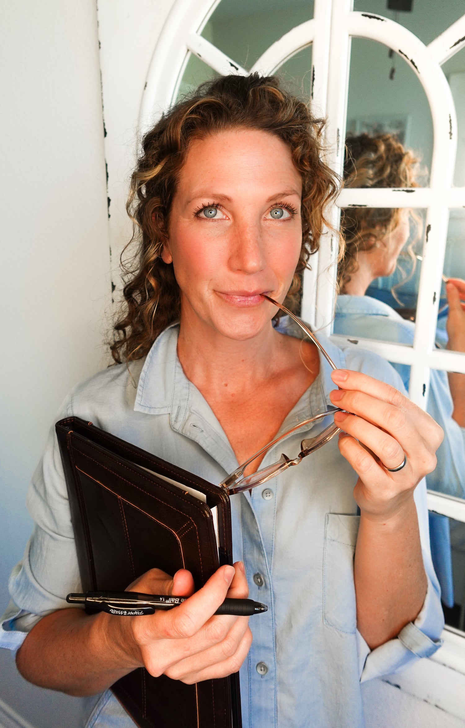 Modern Roots founder and clean and holistic skincare formulator Meg holding her glasses and a portfolio