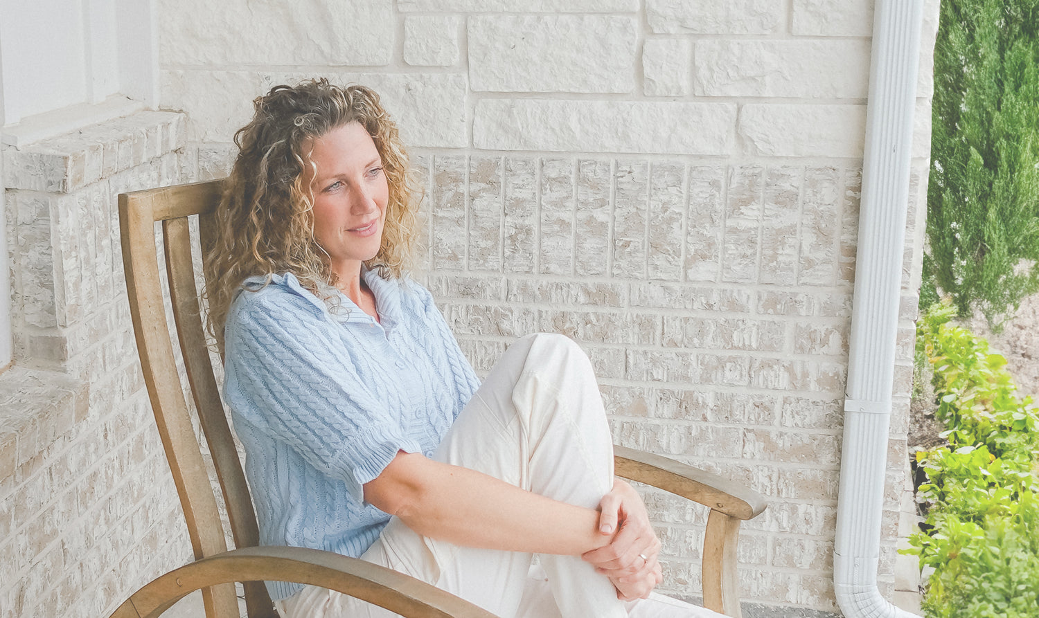 Meg, the founder of clean & holistic skincare brand Modern Roots sitting in a porch rocking chair in a sweater and white pants