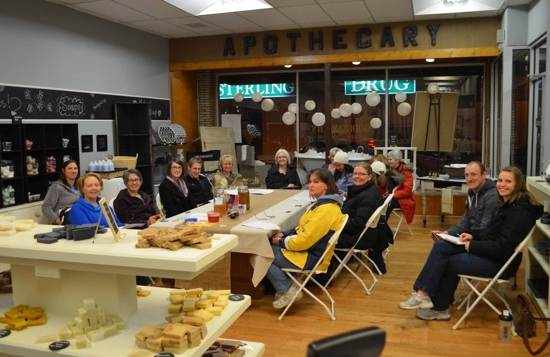 A group of people sitting around tables at a non-toxic refill store surrounded by hand made soap bars.